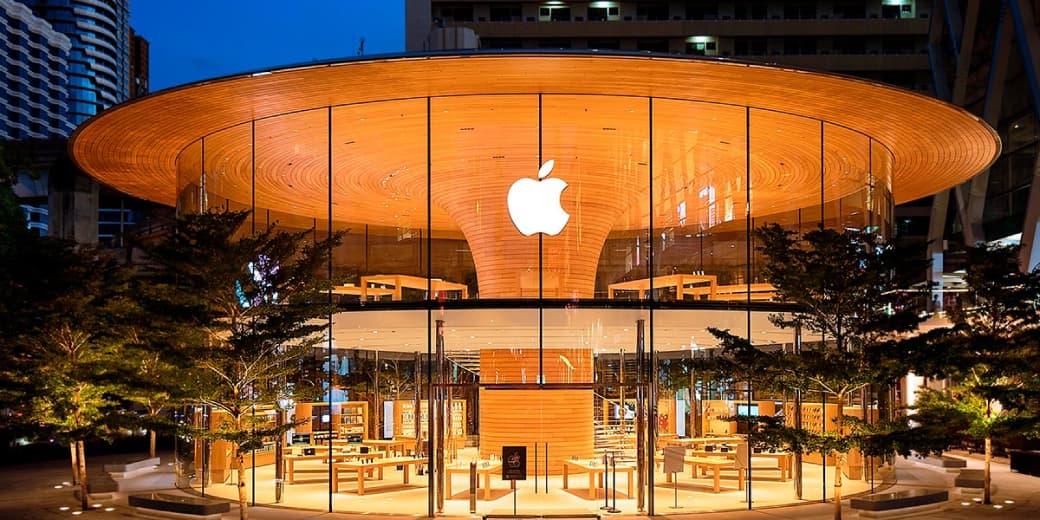 Illuminated glass-front Apple Store with a wooden interior and Apple logo at night.