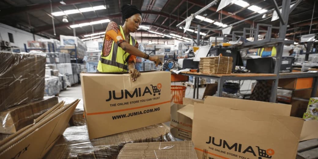 A Jumia warehouse worker packing an order into a branded delivery box.