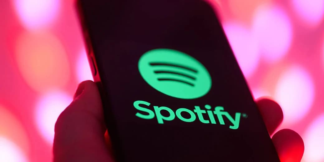 A phone displaying the Spotify app logo against a pink background.