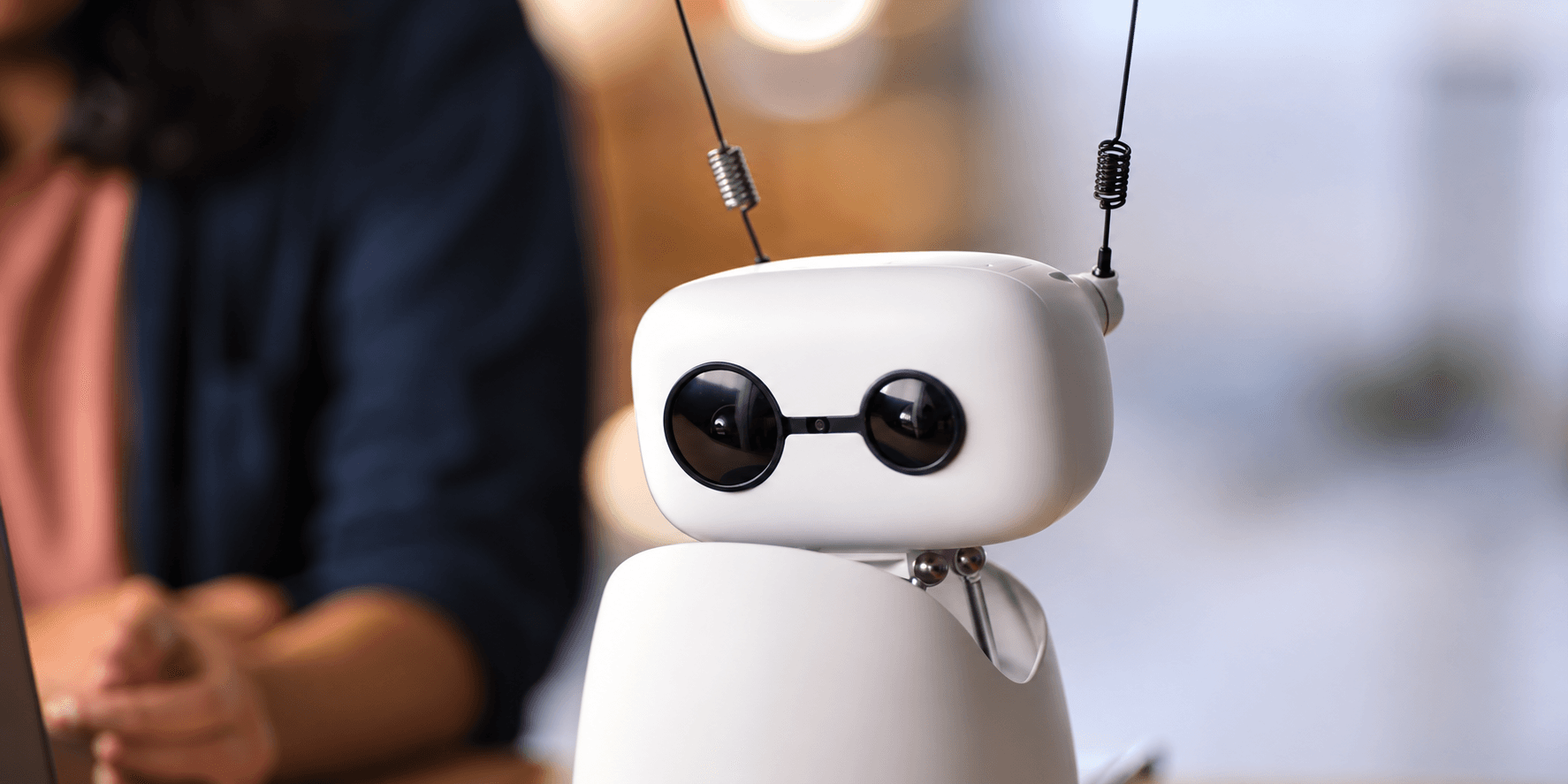 A small white assistant robot beside a person using a laptop.
