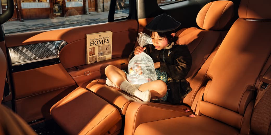 Young passenger seated across the orange rear bench inside the Xpeng G9L cabin.