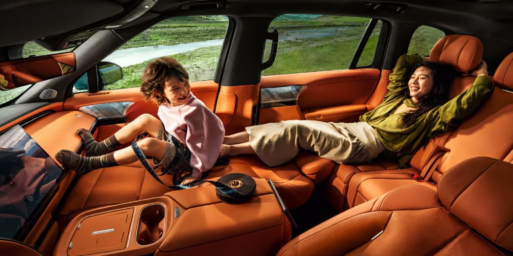Two passengers relaxing across the orange Xpeng G9L cabin seating.