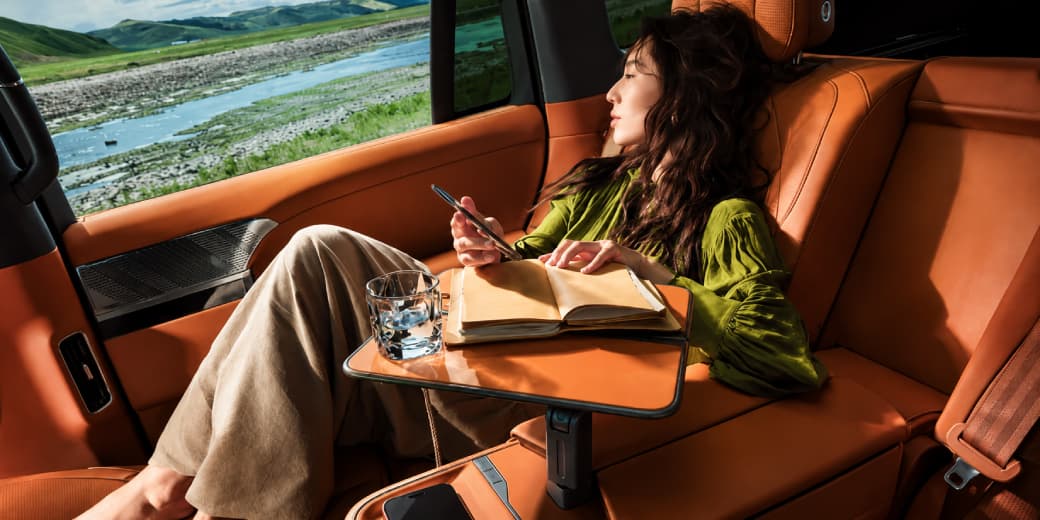 Rear passenger using the folding table inside the orange Xpeng G9L interior.