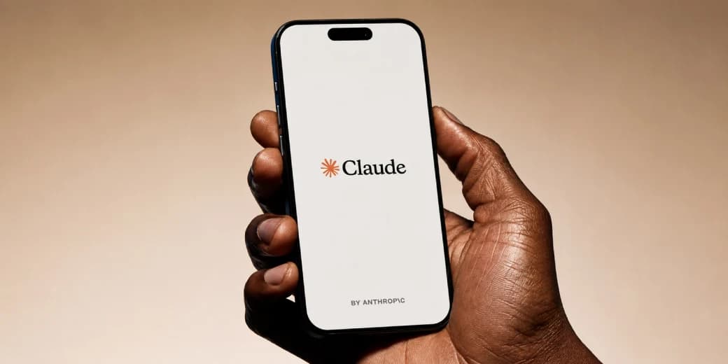A person holding a phone displaying the Claude by Anthropic logo.