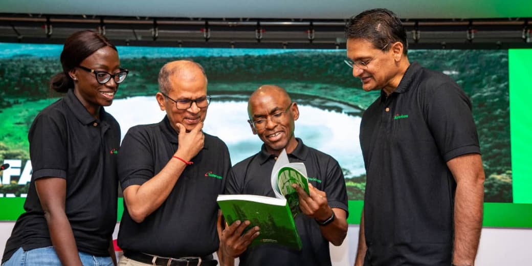 Four Safaricom executives reviewing a green annual report at a company event.