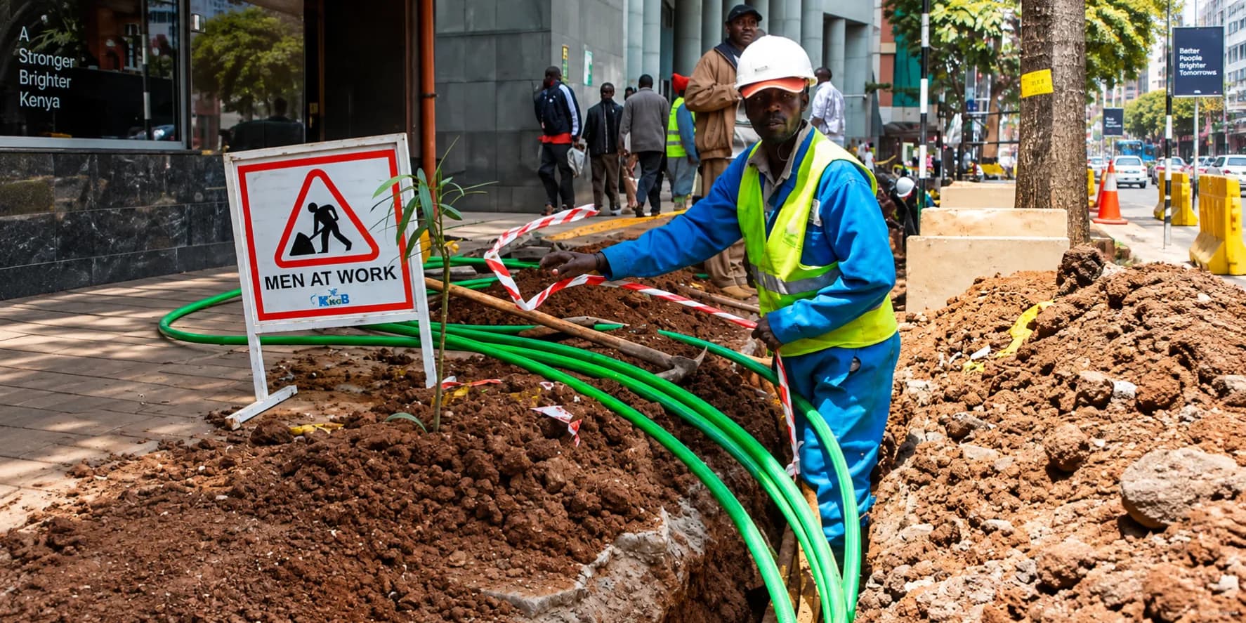 Telecommunications workers installing green fiber-optic conduit in a trench on a Nairobi street.