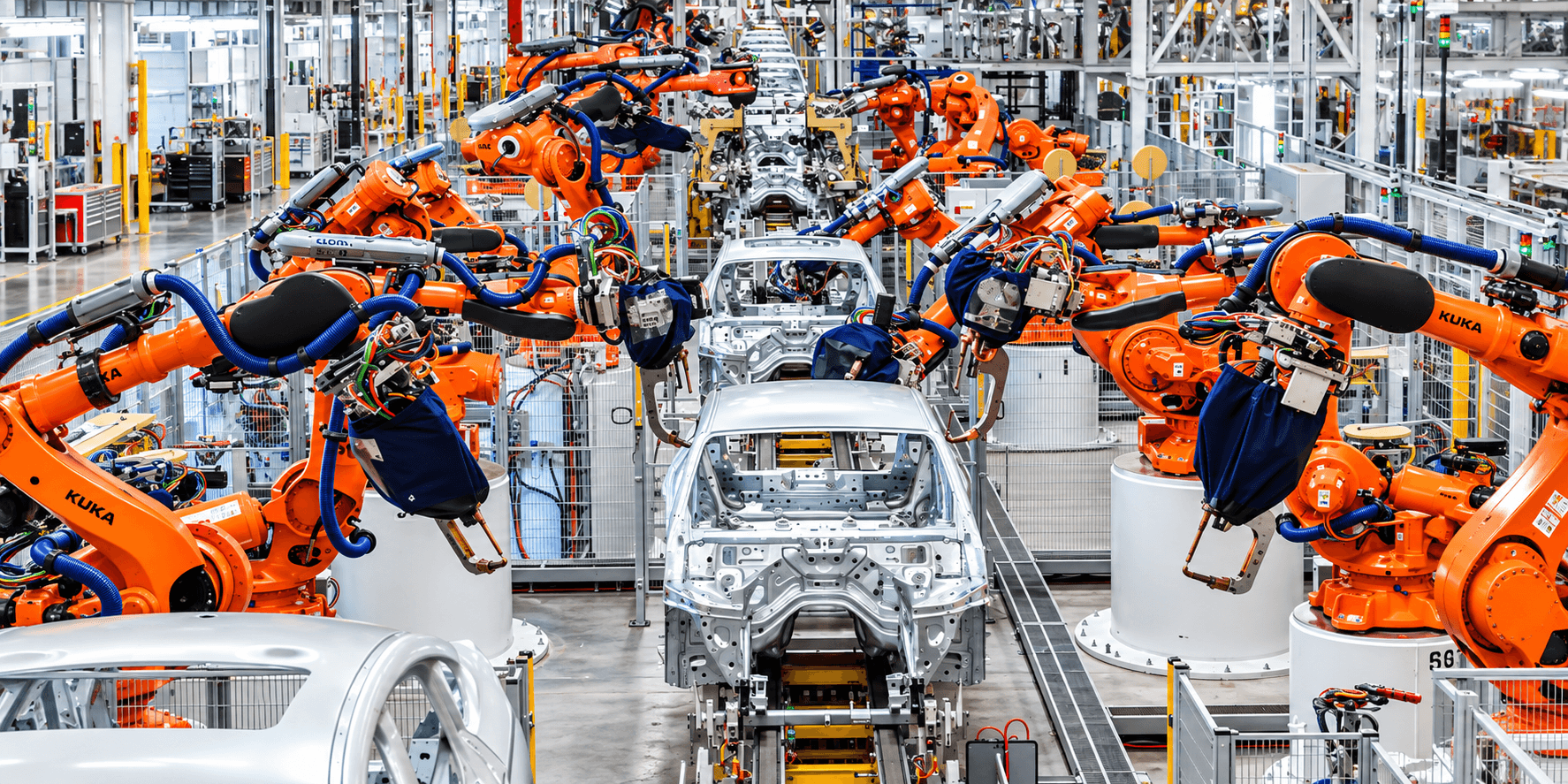 Orange industrial robots working around vehicle bodies on an automotive production line.
